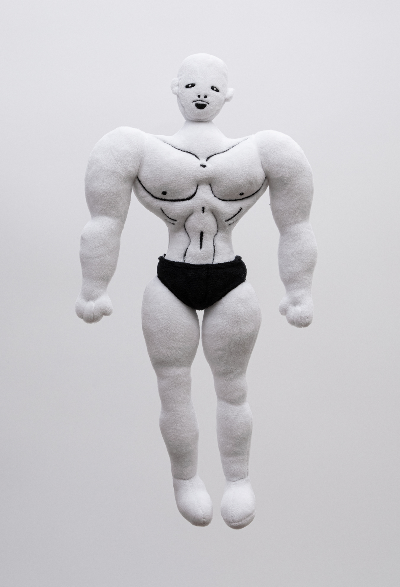Plush figure of a muscular male character with white skin, bald head and black briefs on facing the camera against a white background.